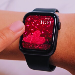 May include: A black smartwatch with a pink glitter background and a large pink heart on the screen. The time is 11:11 and the date is Fri 14.