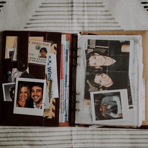 Puede incluir: Agenda de cuero marrón abierto con fotos, documentos y una identificación de Inspector del Estado de Washington. El planificador contiene varias fotos, incluyendo una pareja sonriendo y un grupo de personas. El planificador está abierto sobre una superficie rayada.