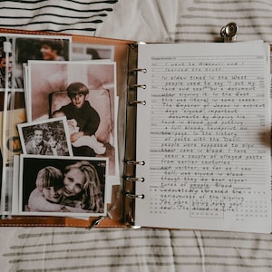 May include: A brown leather journal with handwritten notes and black and white photographs. The journal is open, revealing text and a calendar. The photographs depict people.