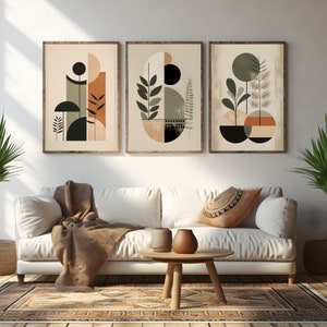 Puede incluir: Tres impresiones de arte abstracto con formas geométricas y follaje en tonos de verde, marrón y beige. Las impresiones están enmarcadas en madera natural y colgadas en una pared blanca sobre un sofá blanco.