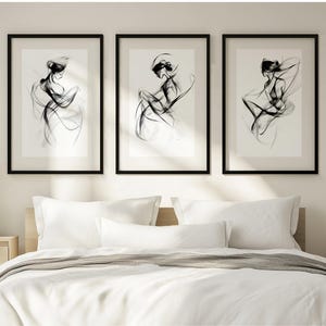 Könnte beinhalten: Drei schwarz-weiße gerahmte Drucke von abstrakten Linienzeichnungen von Frauen. Die Drucke hängen an einer weißen Wand über einem weißen Bett mit weißen Bettwäsche.