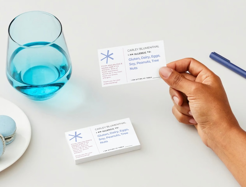 Customizable allergy alert cards.  Includes, name, allergen, restaurant instructions, table number.  Showing both sides with a glass of water and a person holding one of the cards.