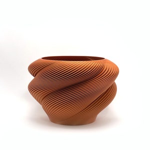 May include: A terracotta-colored ceramic planter with a unique, swirling, ribbed design. The planter is made of a smooth, textured material and has a wide, open top.
