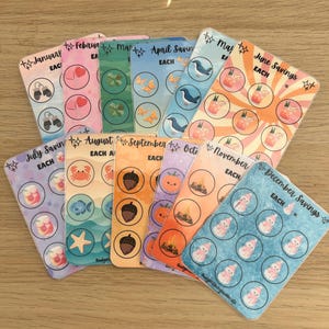 May include: A set of twelve monthly budget planner sticker sheets. Each sheet is decorated with themed illustrations and the text "Each". The stickers are designed for financial planning and savings tracking.