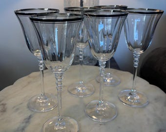 May include: Set of six clear glass wine glasses with a silver rim. The glasses have a fluted design and are perfect for serving wine.