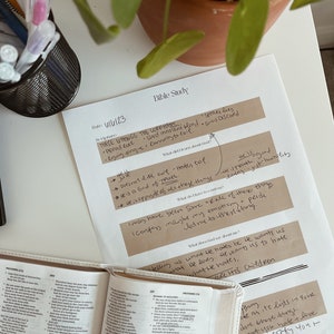 May include: A Bible study setup with an open Bible, handwritten notes, and a potted plant. The notes include the text "THESE THINGS THE LORD HATES" and other scriptural references. Pens are in a black wire cup.