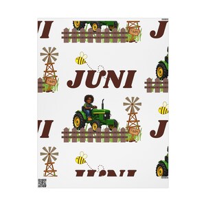 May include: A white fabric pattern featuring a repeating design of a person driving a green tractor, brown wooden fences, windmills with signs labeled Farm, yellow bees, and the letter J, with the name JUNI printed in large brown letters.