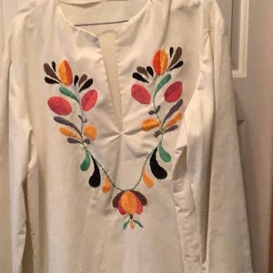 May include: White long-sleeved shirt with colorful embroidered floral design on the front.