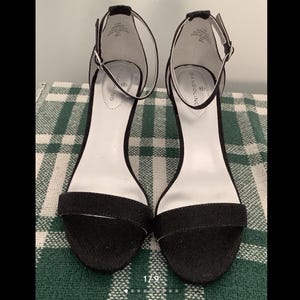 May include: A pair of black suede heeled sandals with ankle straps. The sandals have a white insole and the brand name "Badgley Mischka" is printed on the strap.