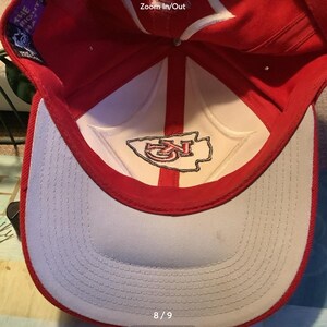 May include: Red and white baseball cap with a white embroidered Kansas City Chiefs logo on the front. The inside of the cap is white with a red brim. The size of the cap is 8/9.