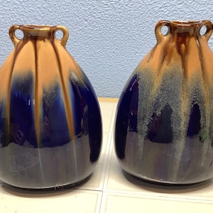 May include: Two blue and brown ceramic vases with handles. The vases have a mottled glaze and a unique, abstract design.