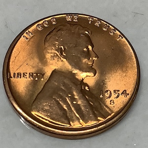 May include: A copper-colored 1954 US penny with the words "In God We Trust" and "Liberty" inscribed around the edge. The year "1954" is visible on the bottom right side of the coin.