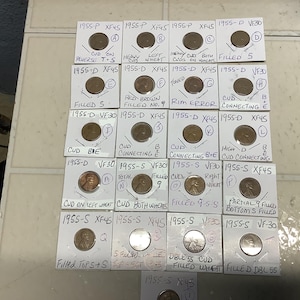 May include: A collection of 1955-P, 1955-D, and 1955-S pennies in protective holders. Each holder is labeled with details such as "CUD ON REVERSE T-S" and "FILLED 5". The coins are in various conditions, including "XF45" and "VF30".