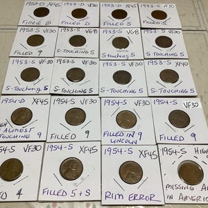 May include: A collection of copper-colored Lincoln pennies, each encased in a white cardboard holder. Handwritten notations on the holders indicate the year, mint mark, and condition of each coin, such as "Filled 9" and "Rim Error."