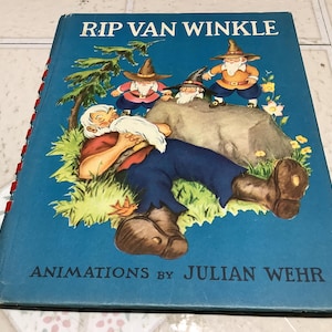 May include: Vintage hardcover book titled "Rip Van Winkle" with illustrations. The cover features a sleeping man in blue pants and a red shirt, surrounded by cartoon gnomes. The book's title and author's name are printed in white.