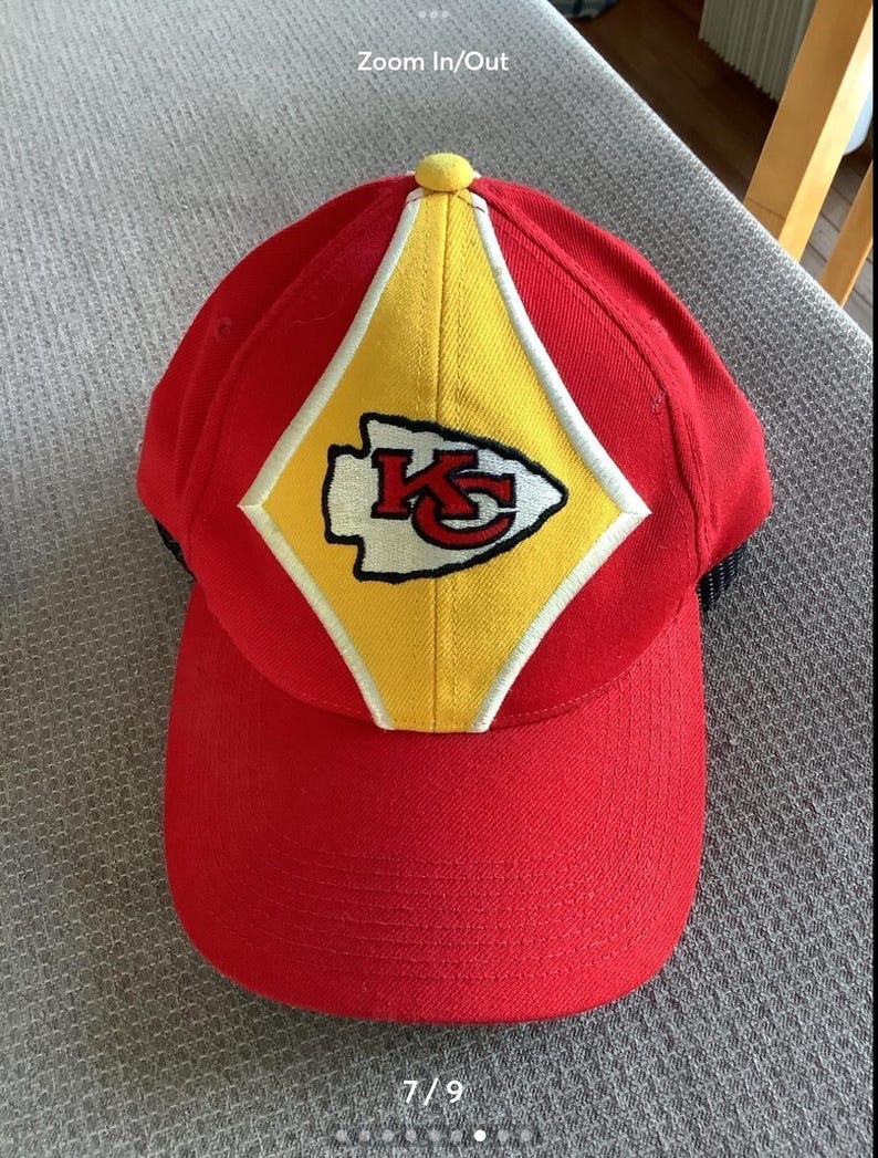 May include: Red baseball cap with a yellow diamond-shaped patch featuring the Kansas City Chiefs logo. The logo is embroidered in white and black with the letters "KC" and an arrowhead.