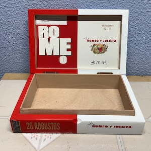 May include: Open wooden cigar box with red and white accents. The box is labeled "ROME" in large white letters on a red background. The lid features "Romeo y Julieta" branding and "Robustos 54 x 5" text.