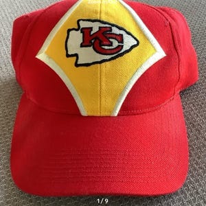 May include: Red baseball cap with a yellow and white diamond-shaped patch featuring the Kansas City Chiefs logo. The logo is white with red and black outlines and the letters "KC" in red.