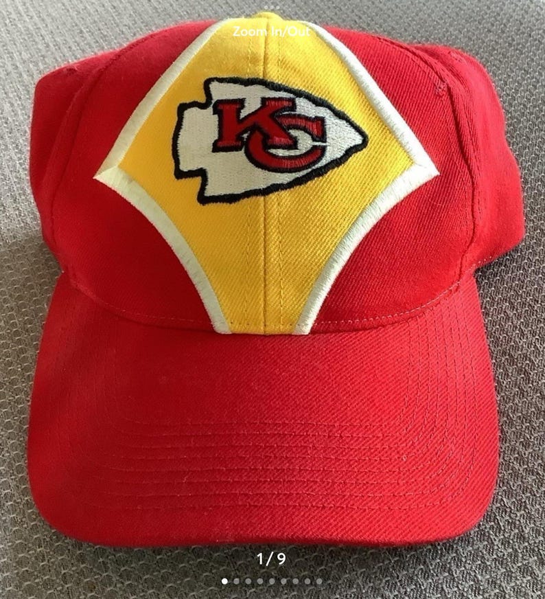 May include: Red baseball cap with a yellow and white diamond-shaped patch featuring the Kansas City Chiefs logo. The logo is white with red and black outlines and the letters "KC" in red.