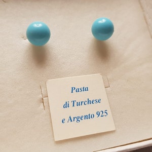 Op de afbeelding: Een paar turquoise en zilveren oorbellen in een witte doos met een label met de tekst "Pasta di Turchese e Argento 925".