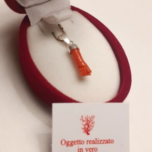 Puede incluir: Un colgante de coral rojo en una caja de terciopelo rojo. El colgante está hecho de coral mediterráneo auténtico y plata 925. La caja tiene una etiqueta que dice "Oggetto realizzato in vero Corallo Mediterraneo e argento 925%" y "Made in Italy".