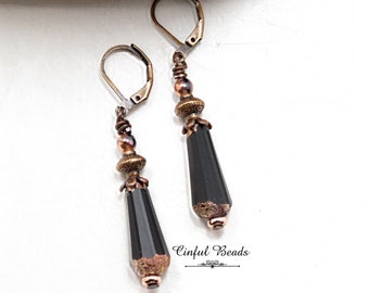 May include: A pair of dangle earrings with black faceted teardrop beads, copper and gold accents, and silver leverback closures. The earrings are approximately 2 inches long.  "Cinflul Beads" is written on the bottom of the image.