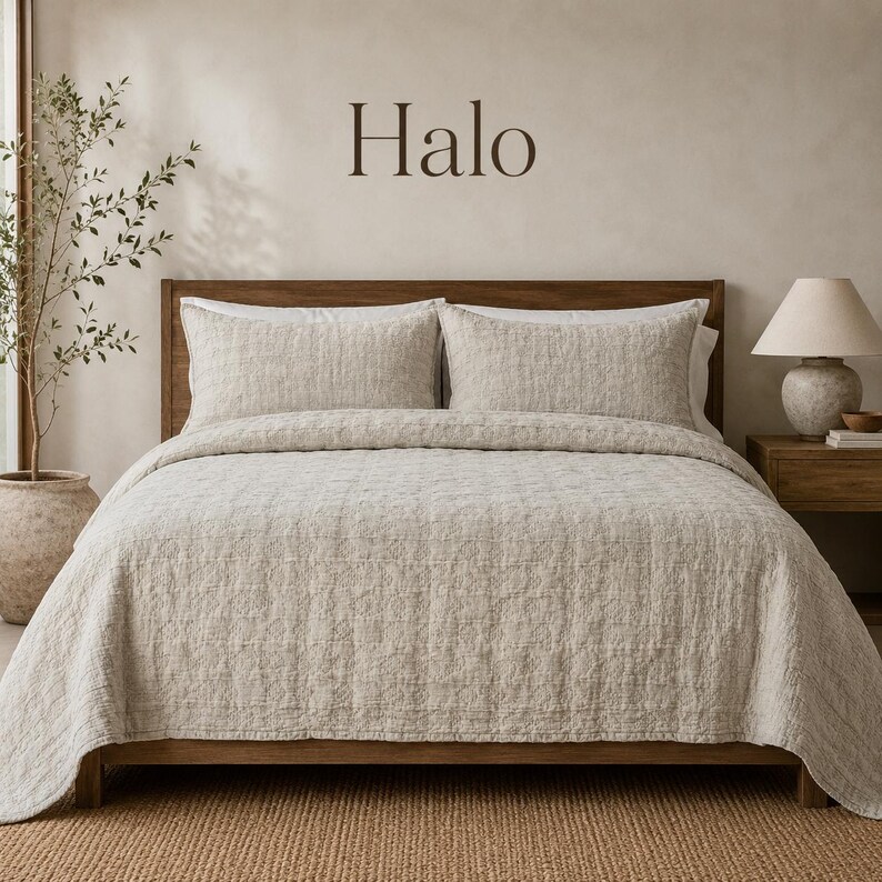May include: A beige textured quilt set on a wooden bed frame with two matching pillows. The word Halo is printed in dark brown letters on the wall above the bed. The bedding features a subtle grid pattern and a soft, woven appearance.