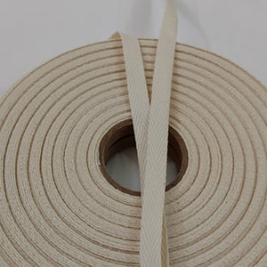 May include: A spool of natural cotton twill tape with a herringbone pattern. The tape is wound tightly on the spool and is ready to be used for sewing, crafting, or other projects.