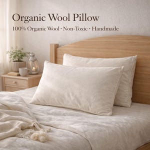 May include: Two off-white organic wool pillows rest on a bed with a light-colored comforter. The headboard is made of light-colored wood. Text on the image reads "Organic Wool Pillow" and "100% Organic Wool • Non-Toxic • Handmade."