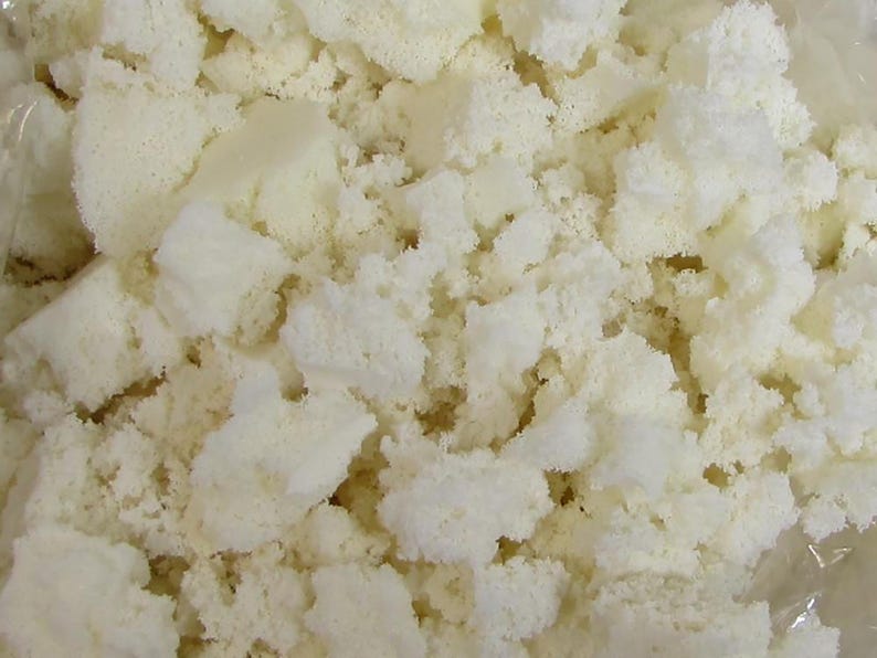 May include: Close-up of a pile of off-white foam pieces. The foam is irregularly shaped, with a porous texture and a slightly uneven surface. The pieces vary in size and are tightly packed together.
