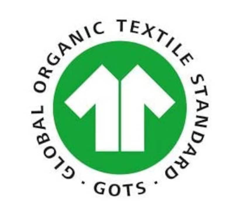 May include: A circular green logo featuring a white stylized t-shirt icon in the center. The text GLOBAL ORGANIC TEXTILE STANDARD is printed in black along the upper circular border, with the acronym GOTS positioned at the bottom center.