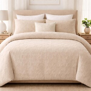 May include: A beige bedding set comprising a duvet cover and several pillows. The duvet cover and two large rectangular pillows feature a raised, geometric octagonal pattern. Two white pillows and one smaller central beige pillow are also included.
