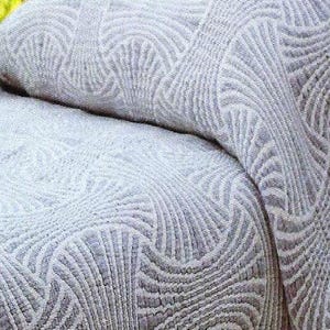 May include: A light grey textile featuring a repeating fan-shaped pattern with raised, textured lines. The fabric displays a consistent geometric design across its surface, with a soft, woven appearance and a monochromatic colour palette throughout.