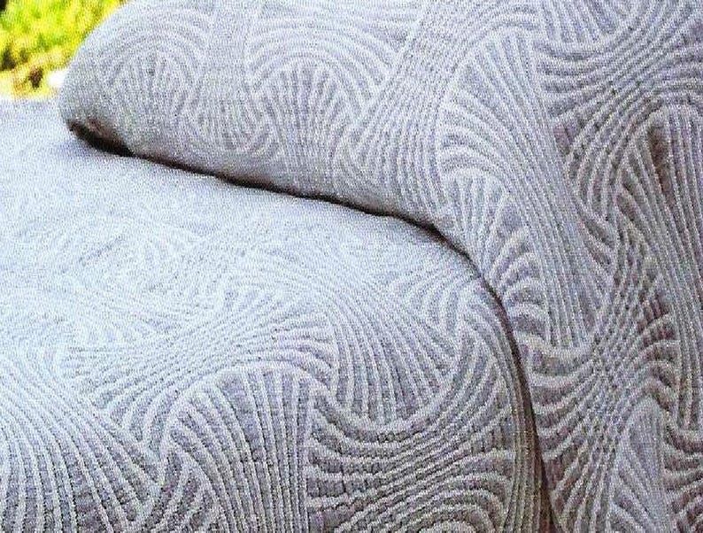 May include: A light grey textile featuring a repeating fan-shaped pattern with raised, textured lines. The fabric displays a consistent geometric design across its surface, with a soft, woven appearance and a monochromatic colour palette throughout.