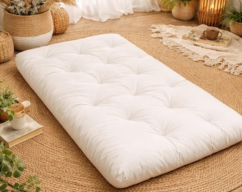 May include: A rectangular white floor mattress featuring a tufted surface with multiple indentations. The mattress is thick and padded, designed for placement directly on the floor, and has a clean, solid white fabric cover throughout.