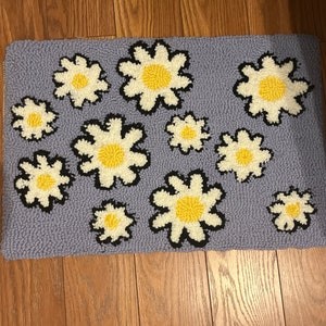 May include: A purple rug with a daisy pattern. The daisies are white with yellow centers and black outlines.