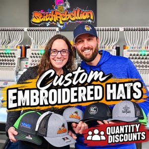 May include: A collection of custom embroidered hats featuring various designs, including logos and text. The hats are displayed in a variety of colours such as grey, black, and blue, with mesh back panels and structured brims, showcasing embroidery services.