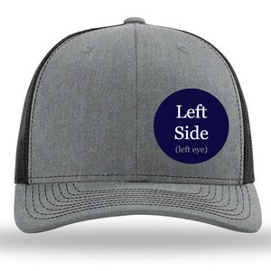 May include: A gray and black trucker hat with a navy blue circle patch that says "Left Side (left eye)".