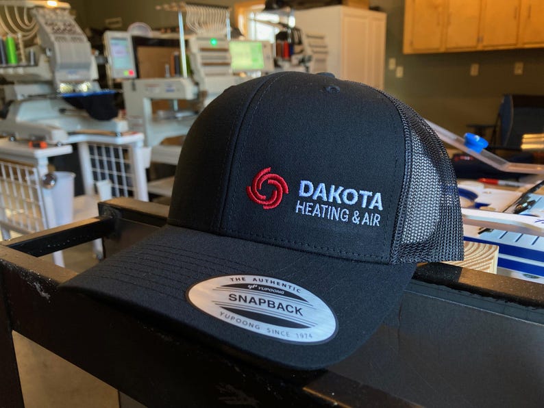 May include: Black and gray trucker hat with a red and white logo that says "Dakota Heating & Air".