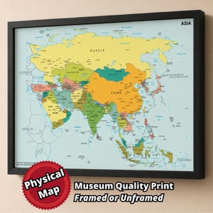 Op de afbeelding: Een ingelijste wandkaart van Azië met een lichtblauwe oceaanachtergrond en veelkleurige landen. De kaart bevat labels voor grote landen zoals Rusland, China en India, met de tekst ASIA en Physical Map.