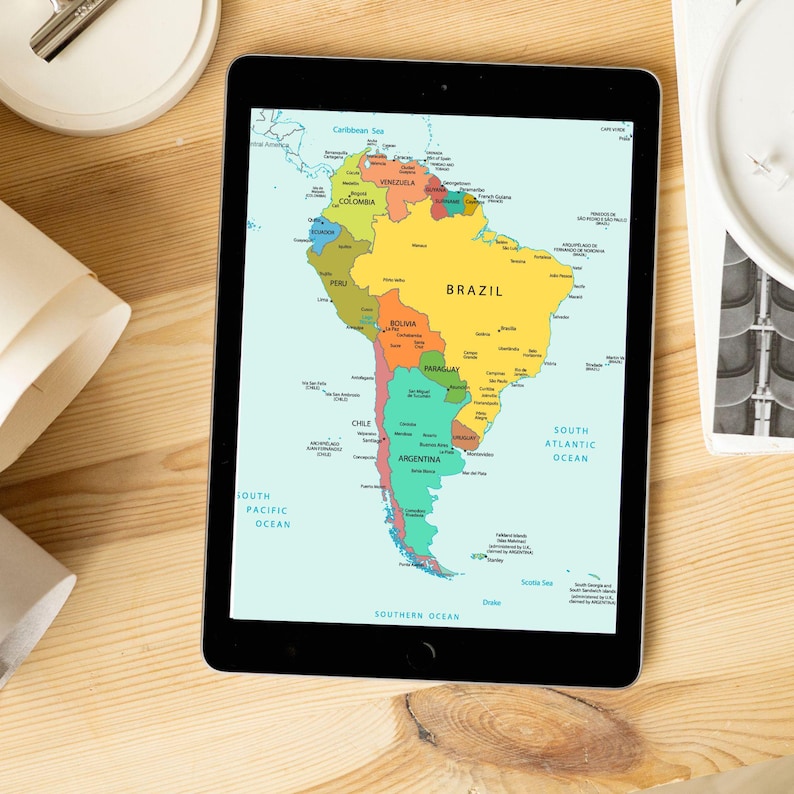 K&ouml;nnte beinhalten: Ein schwarzes Tablet mit einer farbenfrohen Karte von S&uuml;damerika, mit L&auml;ndernamen. Die Karte zeigt Brasilien, Argentinien und andere Nationen, umgeben von Ozeanen. Das Tablet liegt auf einer hellen Holzoberfl&auml;che.