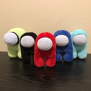 May include: Five crocheted plush toys shaped like the characters from the video game Among Us. The toys are in different colors: green, black, red, blue, and light blue.