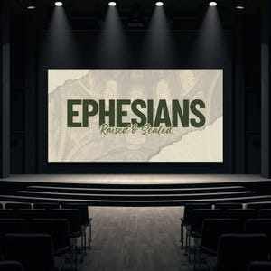 May include: A stage with a large screen displaying the text "EPHESIANS Raised & Seated" in dark green. The background of the screen features a faded architectural design. Rows of black chairs face the stage, and spotlights illuminate the scene.
