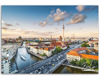 Puede incluir: Una vista aérea de Berlín, Alemania, con la icónica Torre de Televisión en el centro. La ciudad está llena de edificios, calles y un río. El cielo es azul con nubes blancas. El texto "Berlín" está escrito en cursiva blanca en la esquina inferior derecha de la imagen.