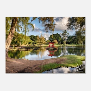 May include: A red wooden bridge with a gazebo on top, spanning a pond in a lush green park. The water reflects the sky and the bridge. The word "Hilo" is written in white cursive on the bottom right corner of the image.
