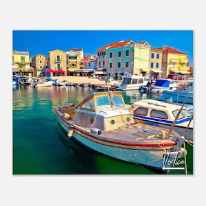 May include: A wooden boat with a white hull and a red stripe is docked in a harbor. The boat has a wooden deck and a small cabin with windows. The boat is surrounded by other boats and colorful buildings.