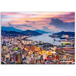 May include: A cityscape print of Nagasaki, Japan, at dusk. The image features a vibrant sunset with shades of pink, orange, and blue over the city and harbor. The word "Nagasaki" is written in white script in the lower right corner.