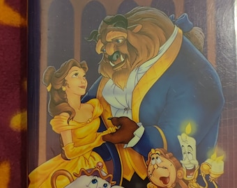 Puede incluir: Una carátula de cinta VHS para la película clásica de Walt Disney "La Bella y la Bestia". La carátula presenta a Bella y la Bestia bailando, junto con los personajes de la Sra. Tetera, Din Don y Lumière.