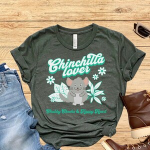 May include: A dark green t-shirt with the text "Chinchilla lover" in a retro font. The shirt features a cartoon chinchilla with the text "Chubby Cheeks & Happy Heart".