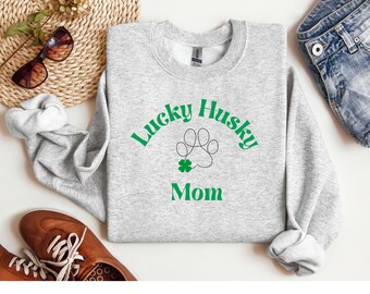 Op de afbeelding: Grijs sweatshirt met de tekst "Lucky Husky Mom" in groene letters met een pootprint en een klavertje vier.